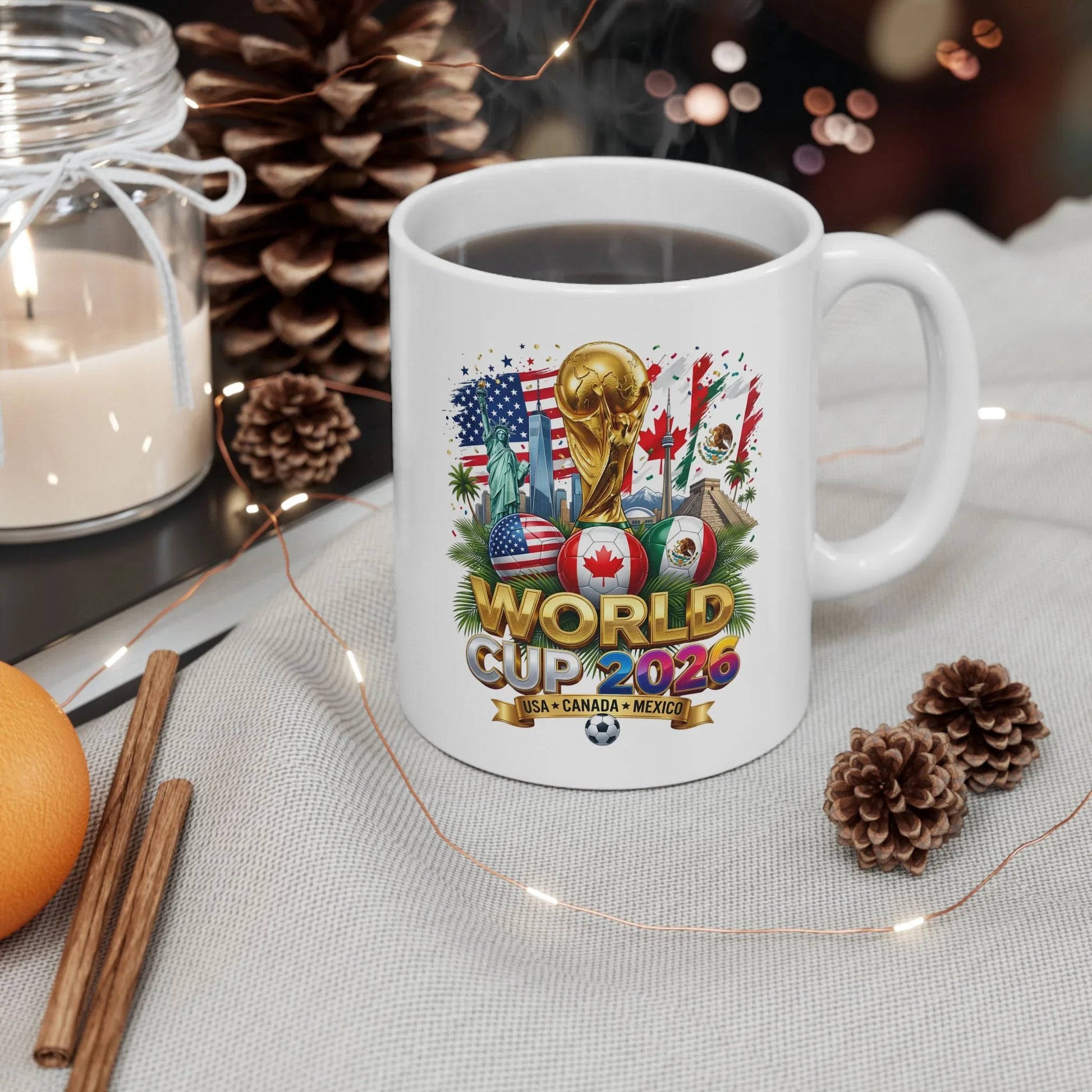 World Cup 2026 trophy and USA Canada Mexico flag soccer balls design on a white mug beside a candle, pinecones and cinnamon