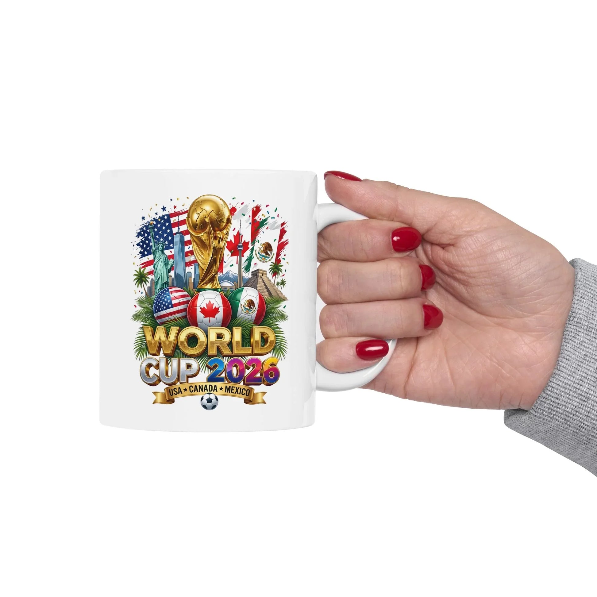 Hand holding a white World Cup 2026 soccer mug showing the gold trophy and USA, Canada, Mexico flag soccer ball design