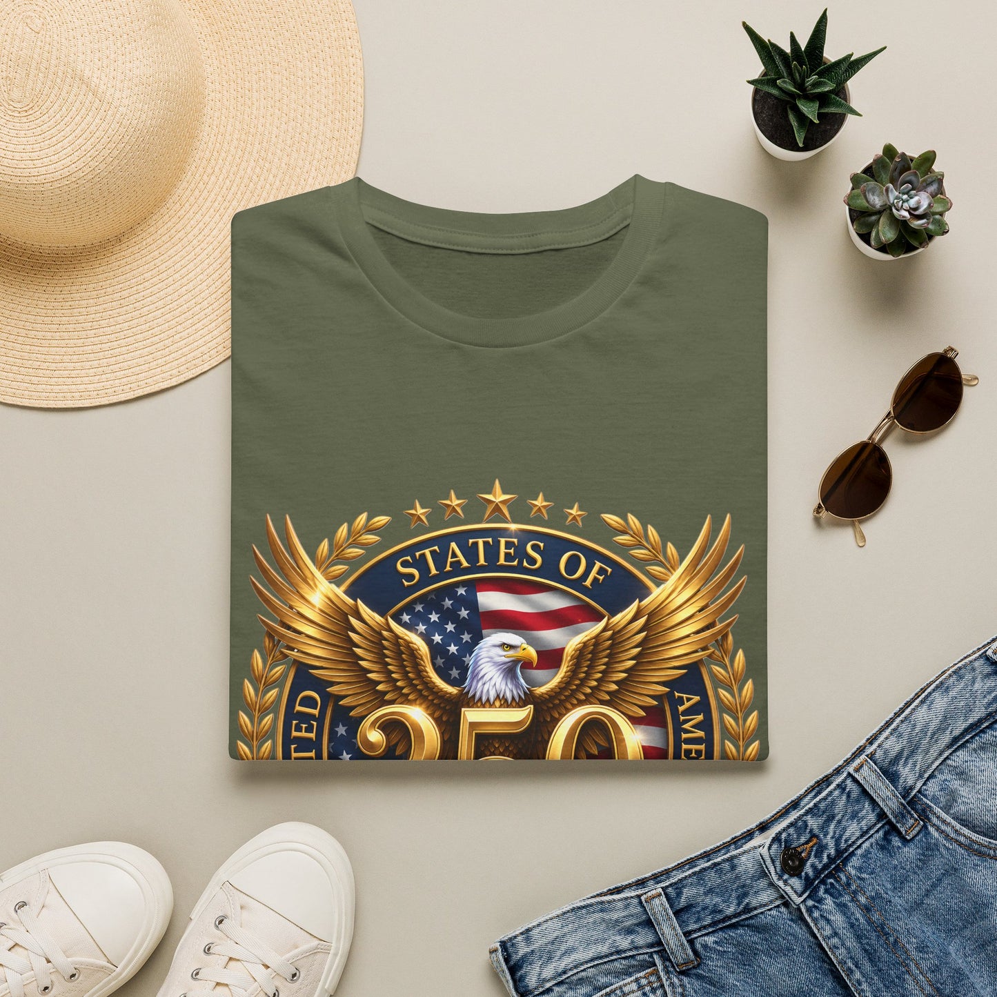 250th Anniversary USA gold eagle crest design on an army-green t-shirt, folded flat lay with a sun hat, plants and jeans