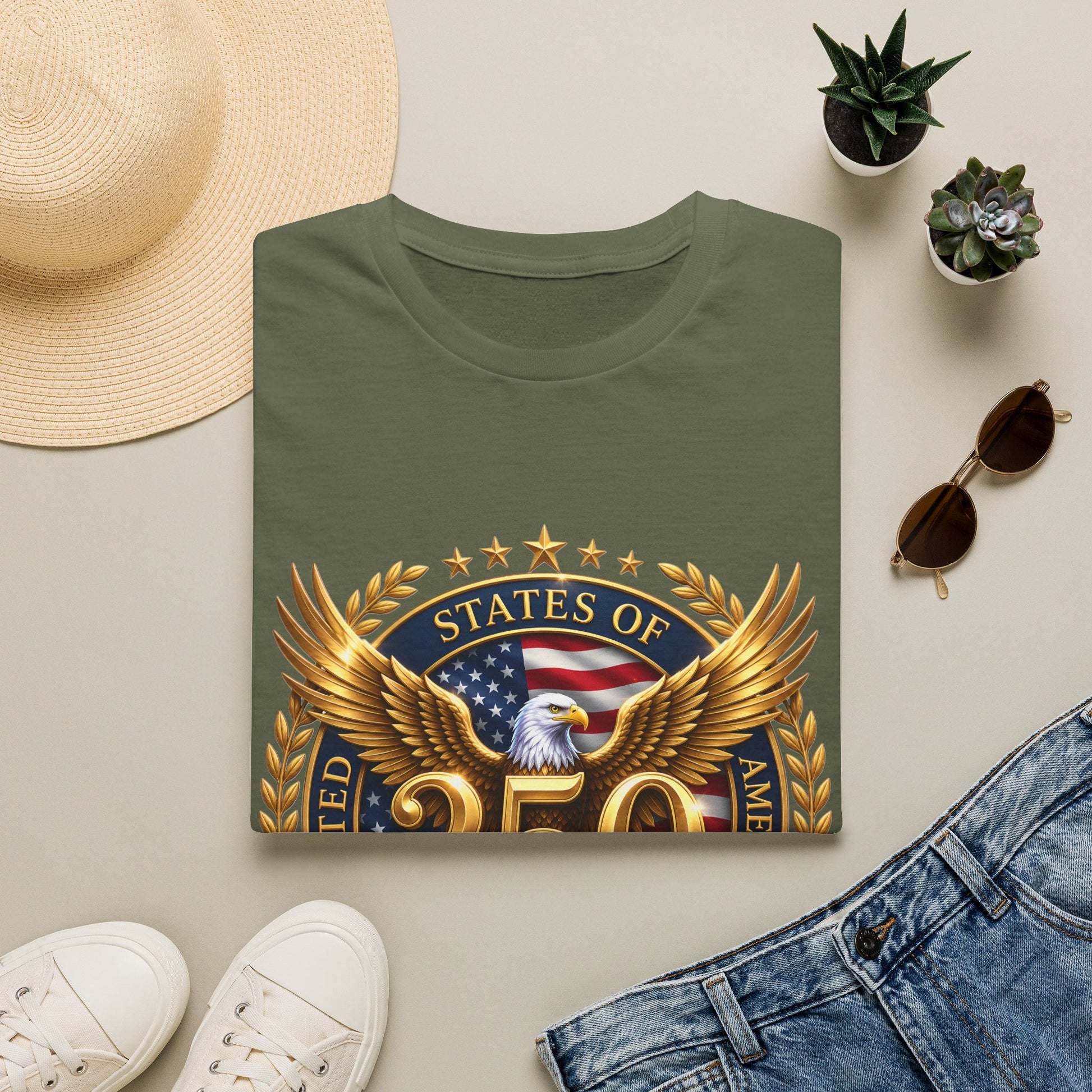 250th Anniversary USA gold eagle crest design on an army-green t-shirt, folded flat lay with a sun hat, plants and jeans