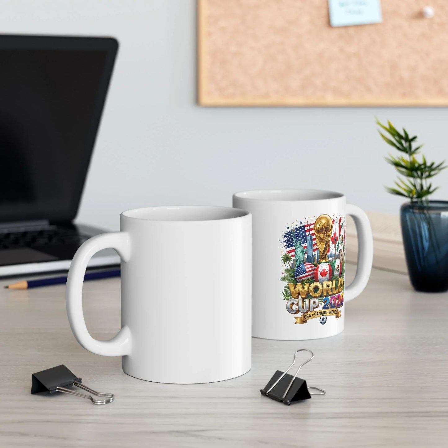 Two white World Cup 2026 soccer mugs on an office desk, one showing the trophy and flag-ball design, the other blank