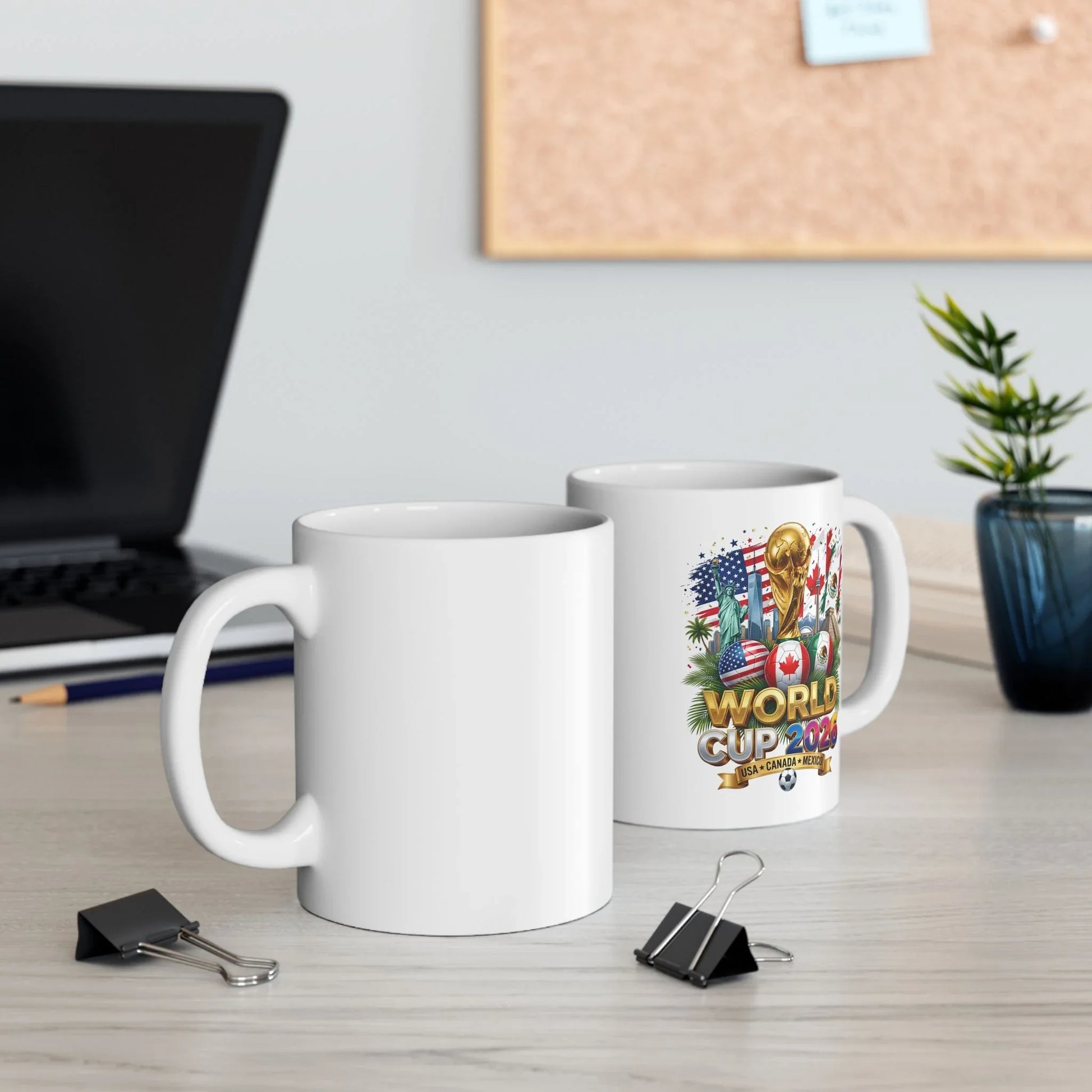 Two white World Cup 2026 soccer mugs on an office desk, one showing the trophy and flag-ball design, the other blank