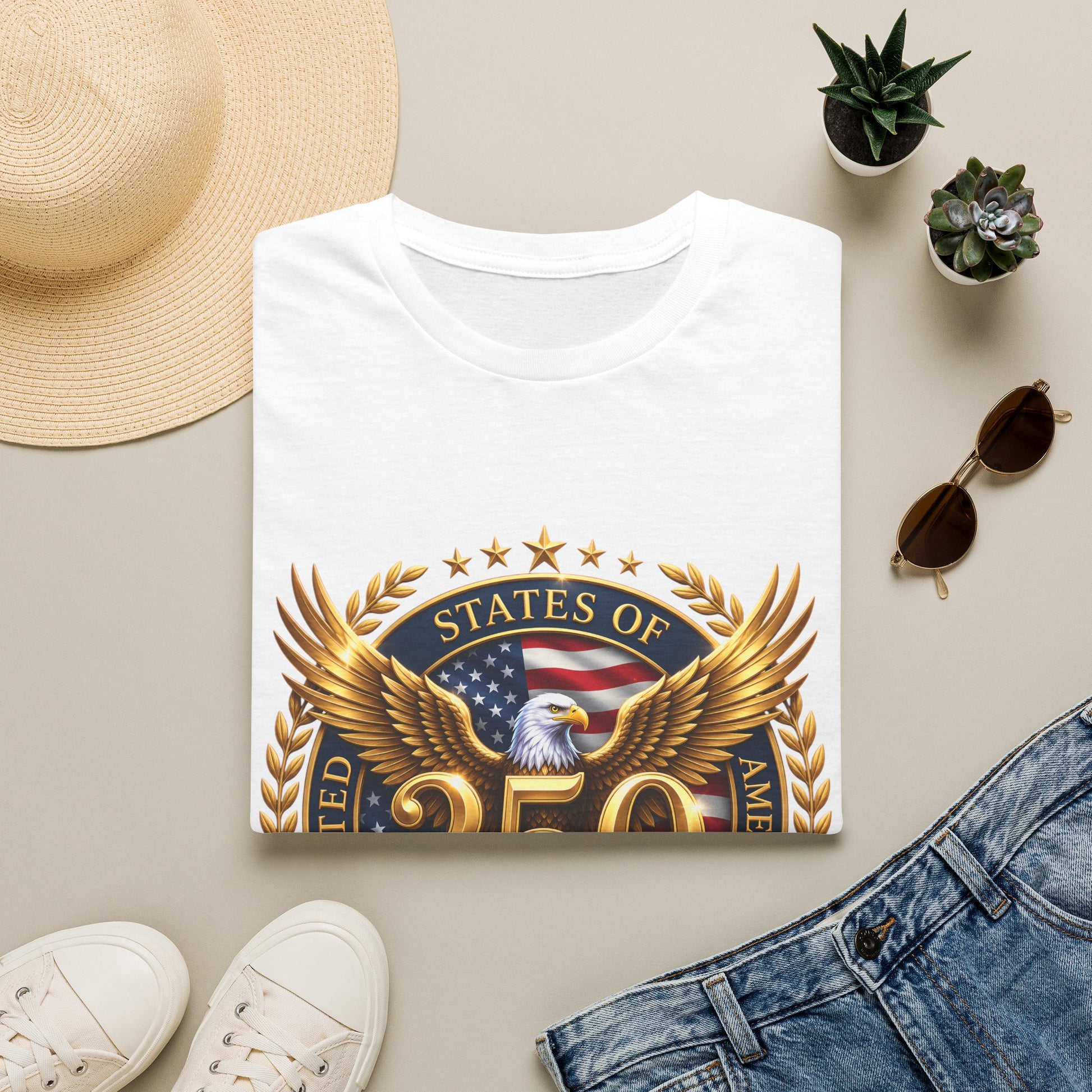 250th Anniversary USA gold eagle crest design on a white t-shirt, folded flat lay with a sun hat, plants and jeans